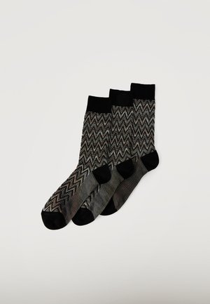 Tres pares de calcetines con patrón de zigzag en negro y gris, con puños, punteras y talones sólidos en negro, dispuestos superpuestos sobre un fondo blanco.