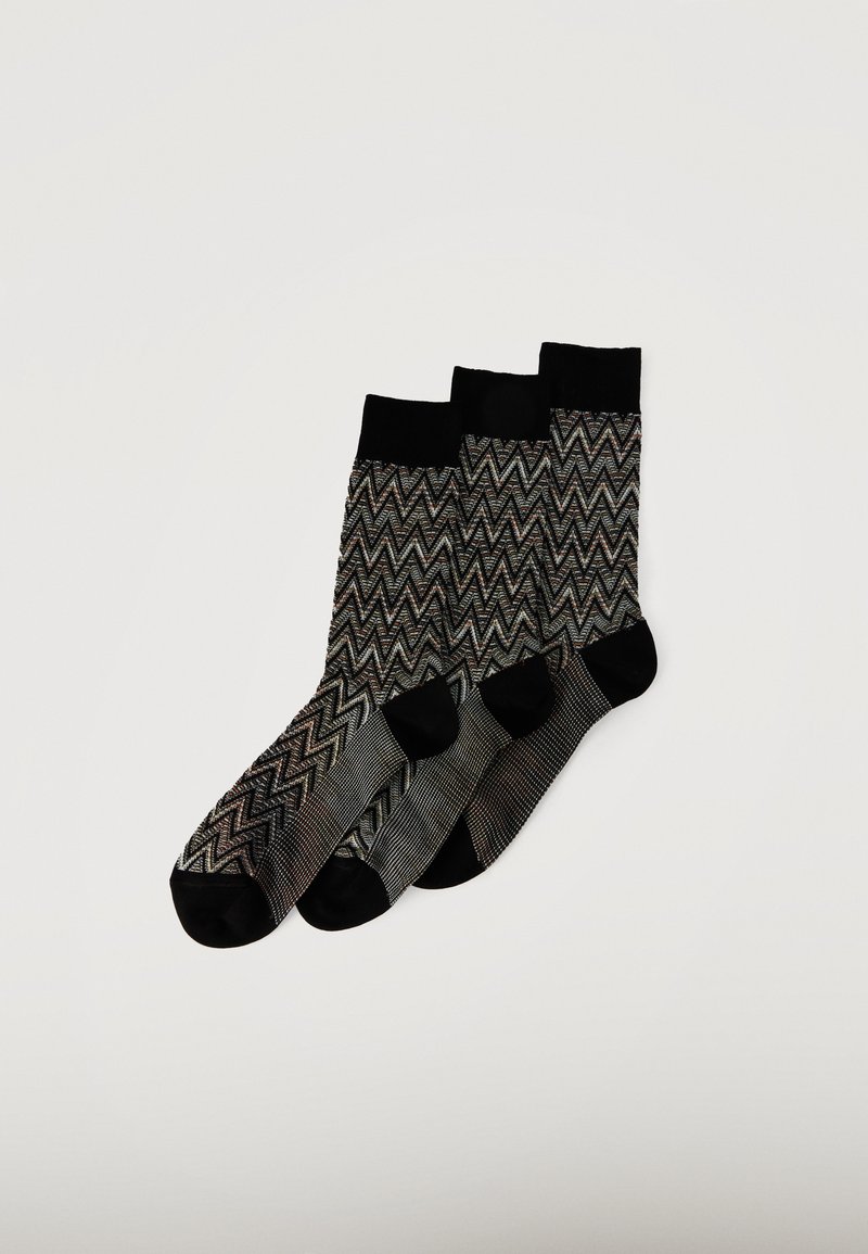 Trois paires de chaussettes à motifs zigzag noirs et gris avec des bords, orteils et talons noirs unis, disposées en chevauchement sur un fond blanc.