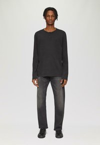 Czarna koszula z długim rękawem i okrągłym dekoltem, z zapięciem na dwa guziki, w połączeniu z ciemnoszarymi dżinsami prostymi oraz czarnymi sneakersami.