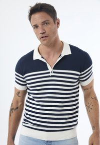 Marineblå og hvid stribet polo t-shirt med hvid krave, korte ærmer og ribbede kanter; har knaplukning og blød strik tekstur.