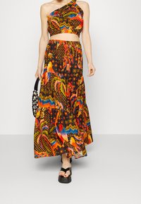 Farverigt todelt sæt bestående af en ensidet crop top og en lang, lagdelt nederdel. Sort baggrund med livlige mønstre af fugle, palmetræer og stjerner.