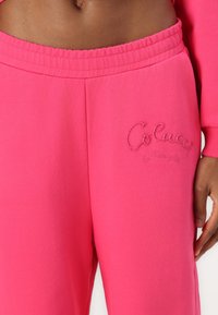Fuchsia joggebukser med elastisk midje, med brodert merkevare på venstre lår og en myk, glatt tekstur.