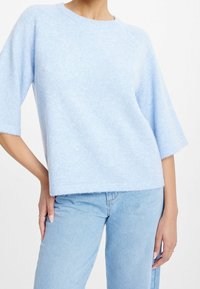 Maglione azzurro chiaro in morbido tessuto lavorato a maglia con scollo arrotondato, maniche a tre quarti e vestibilità comoda. I bordi sono leggermente sfilacciati.