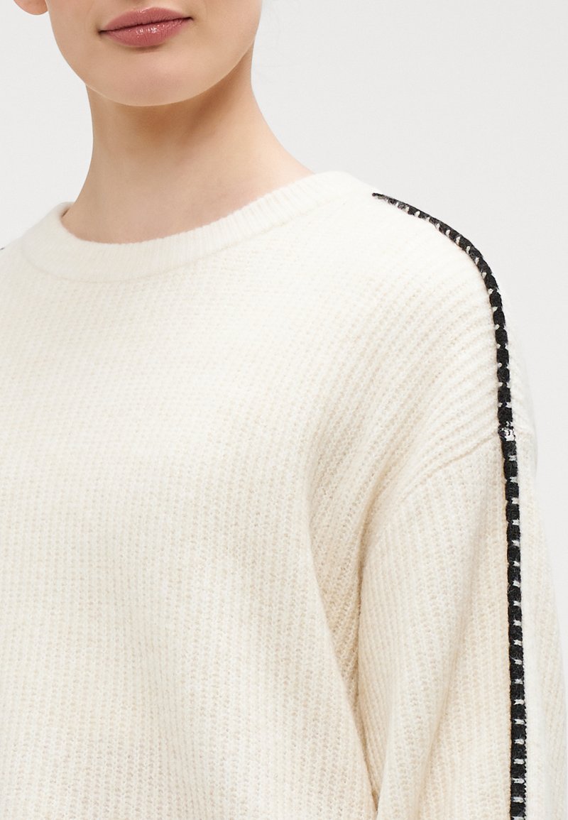 Hellcreme Pullover mit einem strukturierten Strickmuster und schwarz-weißen Streifen an den Schultern. Rundhalsausschnitt, lockere Passform.
