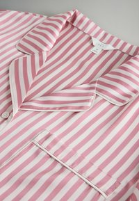 Top de pijama de satén a rayas rosas y blancas con cuello con muesca, bolsillo en el pecho y cierre de botones, mostrado plano sobre una superficie gris.