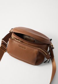 Hnědá kožená crossbody taška s texturou, se zlatým kováním, obsahující přední zipovou kapsu a nastavitelný popruh, vyrobená v kompaktním tvaru.