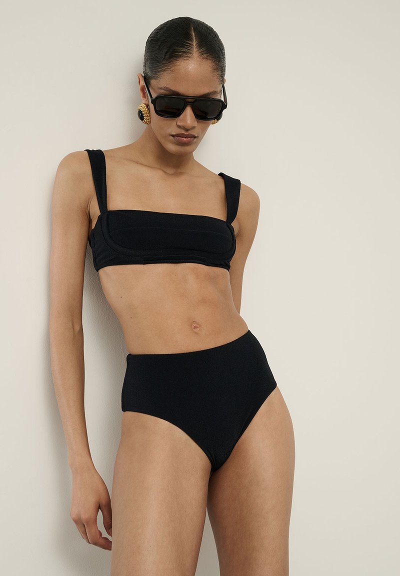 Černý bikini set s strukturálními crop topem s širokými ramínky a vysokými kalhotkami. Hladká, elastická tkanina s minimálními detaily.