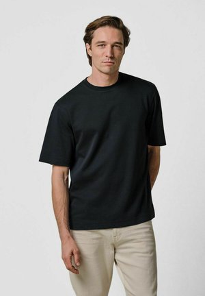 T-shirt nera a maniche corte con scollo a girocollo, realizzata in cotone, con vestibilità morbida e tessuto liscio, abbinata a pantaloni beige chiaro.