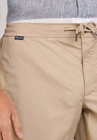 Costumi da bagno beige con vita elasticizzata e cordino, realizzati in tessuto leggero. Presentano un piccolo tag del marchio sul lato.