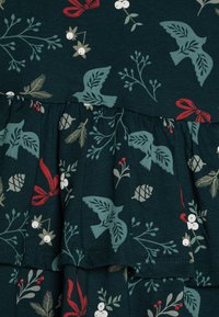 Φόρεμα με λουλουδάτο μοτίβο σε σκούρο πράσινο, με πουλιά, φιόγκους και κλαδάκια σε κόκκινο, λευκό και τυρκουάζ. Το ριχτό στρίφωμα προσθέτει υφή. Υλικό από βαμβακερό μίγμα.