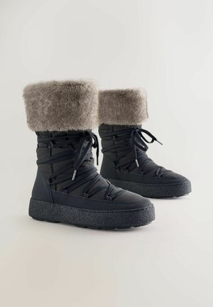 Stivali neri isolati con ampio risvolto in pelliccia sintetica, suola in gomma testurizzata e lacci incrociati per una calzata sicura.