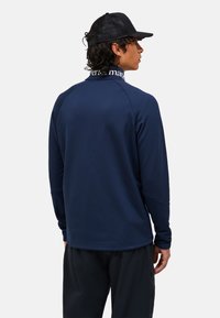 Marineblauwe blouse met lange mouwen, ronde halslijn en raglanmouwen. Gladde textuur met een logoband op de kraag en een relaxte fit.