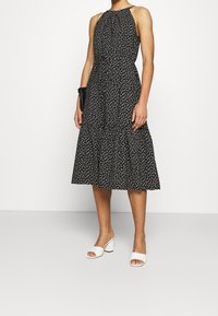 Svart halterneck-klänning med vita prickar, lagrad kjol och elastisk halsringning. Matchad med vita klackskor med blockklack.