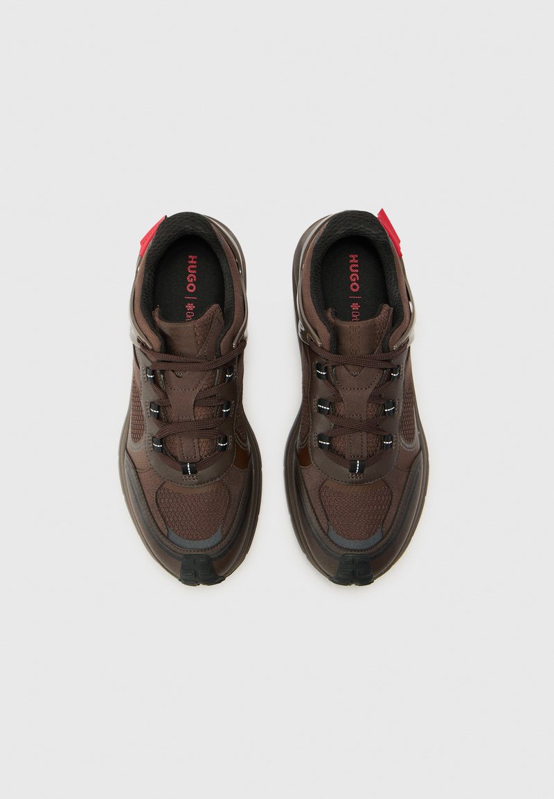 Zapatillas deportivas marrones con parte superior de malla y sintético, detalles en negro, detalles reflectantes y logo rojo en las plantillas, con cordones.