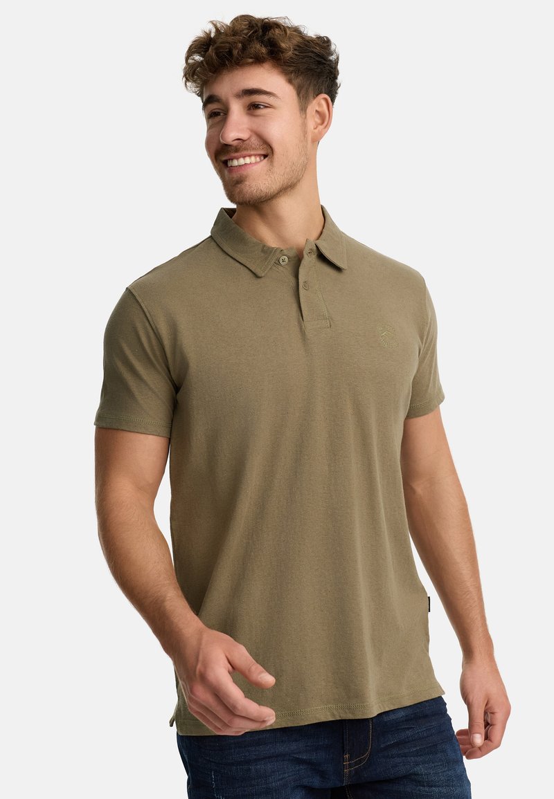 Oliven grøn polo shirt i bomuldsblanding, korte ærmer, to-knaps lukning, lille logo på brystet, parret med mørkeblå jeans.
