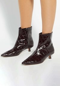 Chocolate brown, glossy ankle boots with a pointed toe, featuring a textured crocodile pattern and small block heel. Side zipper detail included.