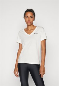 T-shirt bianco in cotone con scollo a V e maniche corte, con un piccolo logo rosso Champion sul petto e un dettaglio sulla manica.