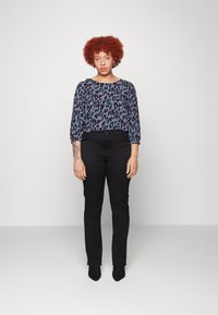 Pantalones negros de cintura alta combinados con una blusa suelta y estampada que presenta un estampado de leopardo púrpura y azul y mangas 3/4.