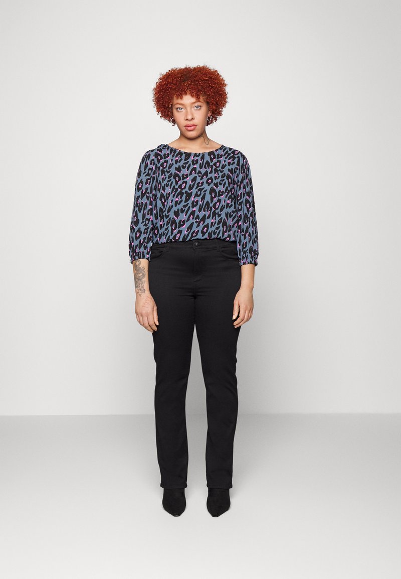 Pantalones negros de cintura alta combinados con una blusa suelta y estampada que presenta un estampado de leopardo púrpura y azul y mangas 3/4.