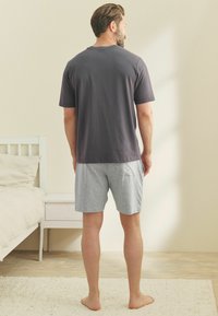 Grå bomulls T-shirt med rund halsringning, tillsammans med ljusgrå shorts. Szenen visar ett minimalistiskt sovrum med naturligt ljus.