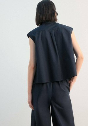 Dark navy sleeveless top with a high collar, featuring a relaxed fit and back pleat detail. Paired with matching loose trousers.