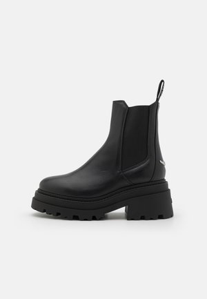 Black chelsea boots made of smooth leather with elastic side panels, a thick, ridged rubber sole, and a pull tab at the back.