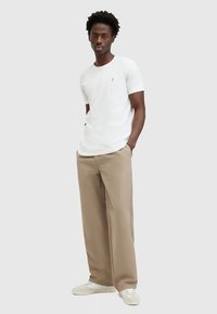 Baltas medvilninis marškinėlis trumpomis rankovėmis, derinamas su smėlio spalvos plačiomis kelnėmis ir baltais sportiniais bateliais. Paprastas dizainas, be išraiškingų raštų.