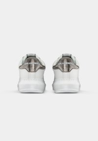 Et par hvite sneakers med sølvfargede hæltrekk og "KARL LAGERFELD"-merking sett fra baksiden på en enkel hvit bakgrunn.