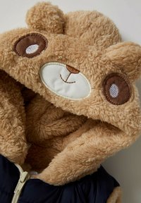 Brauner Teddybär-Hoodie, gefüttert mit Plüschmaterial, mit gestickten Augen und Nase, kontrastiert mit einer navyblauen Außenschicht und Reißverschluss.