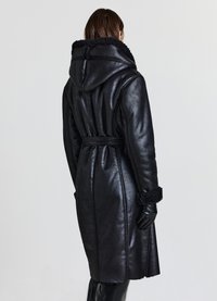 Cappotto in pelle nera con cappuccio, caratterizzato da una vita con cintura, dettagli in shearling al colletto e ai polsini, e una finitura morbida e liscia.