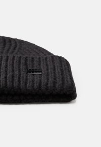 Knitted black wool beanie with ribbed texture and folded brim. Features a small black logo tag on the front.