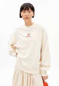 Crème oversized sweatshirt met rood geborduurd "ARMEDANGELS" logo en bloemenontwerp. Zachte stof, ontspannen pasvorm en geribbelde manchetten.