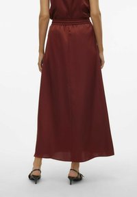 Bordeaux maxi rok met een elastische tailleband, gladde satijnen textuur en een vloeiende silhouet; gecombineerd met zwarte hoge hakken sandalen.