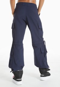 Navy cargo pants made of durable fabric featuring multiple side pockets, adjustable drawstrings at the cuffs, and a relaxed fit.