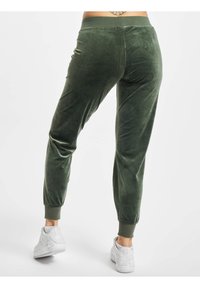 Gröna velour joggers med avsmalnande ben och ribbade muddar; elastisk midja. Kombinerat med vita sneakers. Slät yta, mjukt avslut.