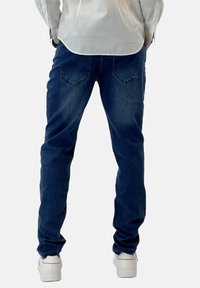 Jeans de mezclilla azul oscuro con un corte recto, que cuentan con dos bolsillos traseros y costuras sutiles, combinados con zapatillas blancas.