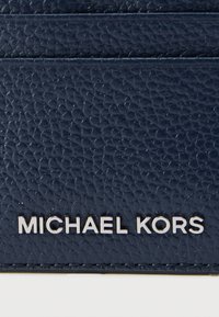 Granatowy teksturowany skórzany etui na karty z widocznym wytłoczonym na przodzie srebrnym logo „MICHAEL KORS”, wyposażonym w wiele przegródek na karty.