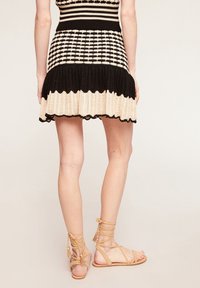 Abito lavorato a maglia nero e crema con un motivo a quadri, orlo svasato e bordi ondulati, abbinato a sandali beige con lacci.