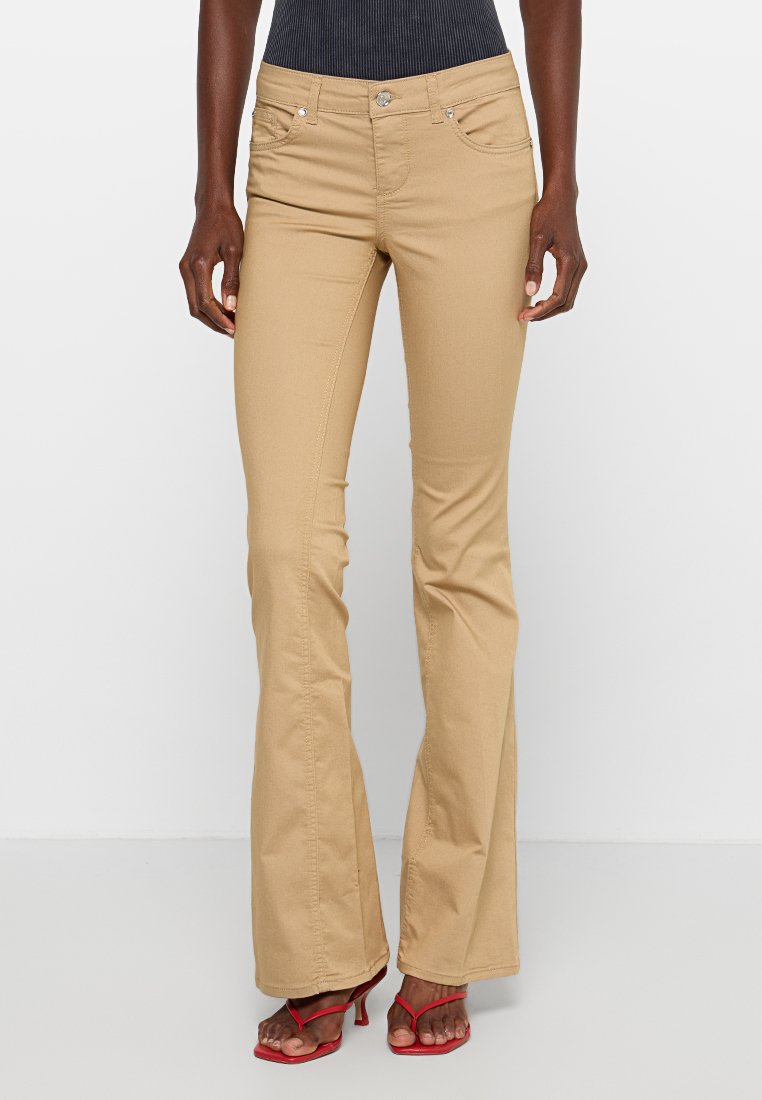 Khaki flare jeans met een gladde textuur, voorzien van voorzakken en een enkele knoopsluiting. Gepaard met rode sandalen.