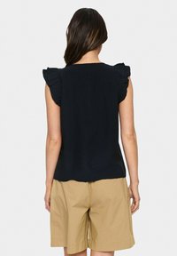 Top nero senza maniche con dettagli a volant sulle spalle, abbinato a pantaloni corti beige chiaro. Tessuto liscio, design semplice e senza motivi visibili.