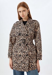 Trench coat de estampado de leopardo con cintura ceñida por un cinturón, diseño de doble botonadura y botones negros. Fabricado en tela ligera con una textura suave.