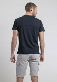 T-shirt en coton bleu marine à manches courtes, vu de dos. Association avec un short cargo gris clair comportant des poches latérales.