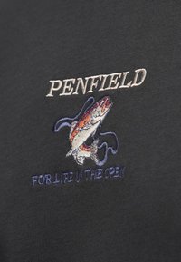 Czarna tkanina z wyhaftowanym napisem "PENFIELD" nad kolorowym wzorem ryby oraz niebieskim napisem "FOR LIFE IN THE OPEN" poniżej.