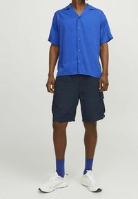 Camisetta azzurra a maniche corte con colletto, con chiusura a bottoni sul davanti; abbinata a pantaloni cargo blu navy e sneaker bianche. Tessuto morbido, vestibilità casual.