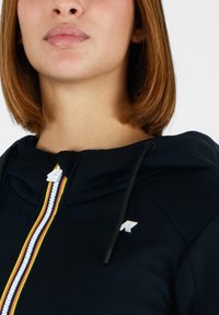 Felpa nera con cappuccio e zip frontale, caratterizzata da una striscia multicolore al centro e accenti di logo bianchi sul petto e sulla zip.