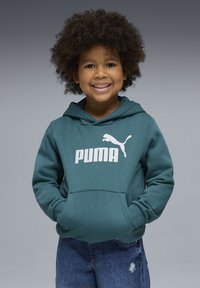 Sweat à capuche bleu sarcelle avec une poche kangourou et un logo Puma blanc sur la poitrine, associé à un jean en denim bleu avec des détails d'ourlet effiloché.