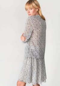 Abito floreale grigio trasparente con maniche corte, scollo rotondo e orlo a strati. Presenta un motivo delicato e un tessuto leggero e fluido.