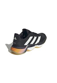 Zapatilla deportiva negra con rayas blancas, que presenta una parte superior texturizada, un cuello acolchado y una suela de goma con un degradado en tonos naranja y amarillo.