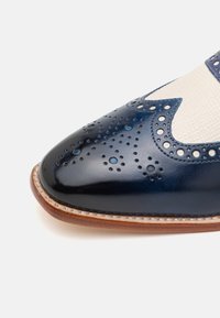 Scarpa in pelle blu con design brogue caratterizzato da perforazioni, finitura liscia, pannello in tessuto beige a contrasto e bordatura marrone.