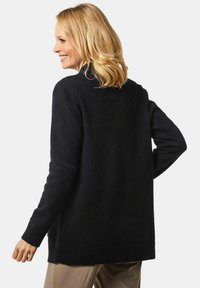 Schwarze Strickjacke mit lockerer Passform, gerippten Bündchen und Saum. Verfügt über einen hohen Kragen und lange Ärmel. Glatte Textur und klassisches Design.